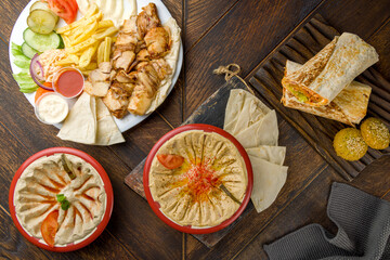 Shawarma on a plate, shawarma on board with falafel, hummus with pita, mutabal top view on wooden table
