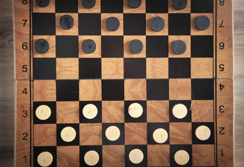 Checkers game on checkerboard in wooden background.
