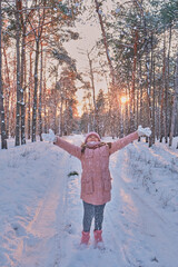 Little girl in pink jacket and knitted hat catching snowflakes in winter park