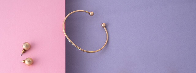 Panoramic shot of golden with diamonds bracelet and earrings pair on pink and purple with copy space