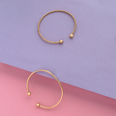 Top view of two golden bracelets on pink and purple slanted paper background