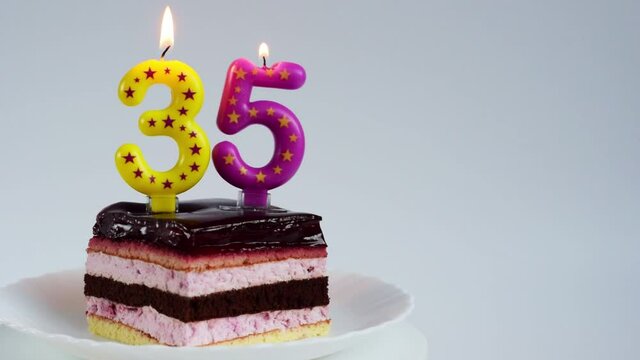 Appetizing birthday cake with burning candles for 35th anniversary on a white rotating plate