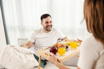 A happy man having breakfast in the bed brought by his wife at their cozy home.