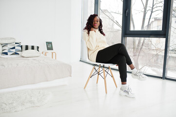 African woman in hoodie sit on chair at home.