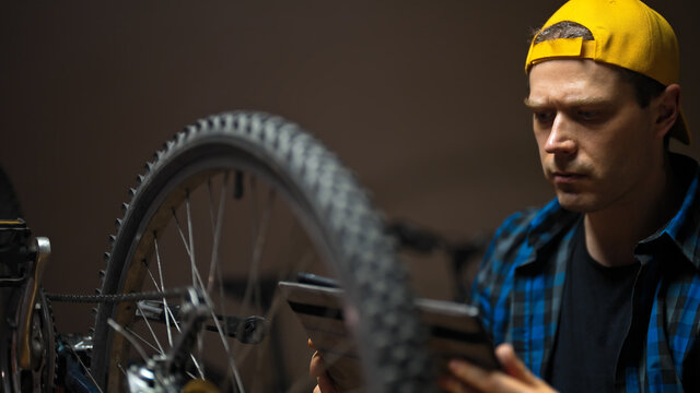 Master with tablet pc examines wheel of the bicycle. Bicycle repair workshop.