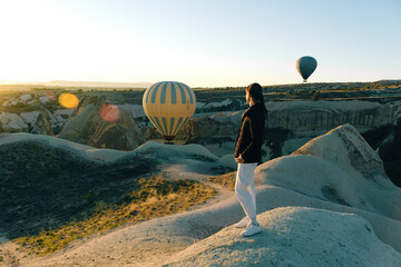 Young woman watching the sunrise and hot air balloons taking off over valley in Cappadocia, Goreme, Turkey