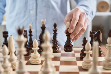 Chess. Black bishop move, chess pieces are sitting on the church board. Handmade carved chess set from natural wood. The grandmaster holds the piece and takes a step
