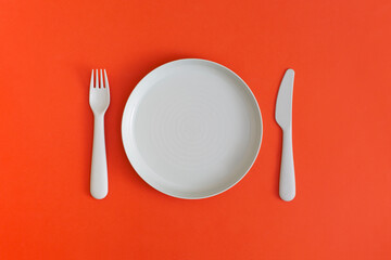 Plate with fork and spoon on a red background. Top view. Flat lay.