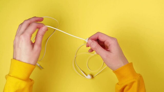 Hands of young woman unravel white headphones for smartphone on bright yellow background