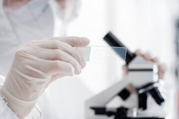 blurred scientist holding laboratory slide while working with microscope.