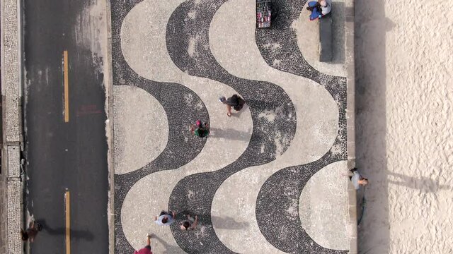 Top down aerial view of people walking on the iconic Copacabana Beach mosaic sidewalk in Rio de Janeiro, Brazil.	