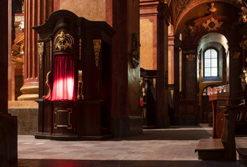 Confessional lit up in red, priest inside, baroque interior of the parish church, Poznan, Poland,