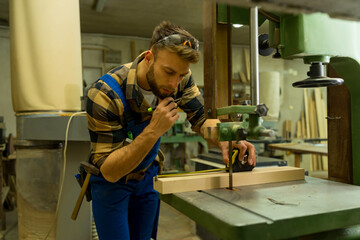 Handsome carpenter preparing, measures and cutting boards on cutting machine