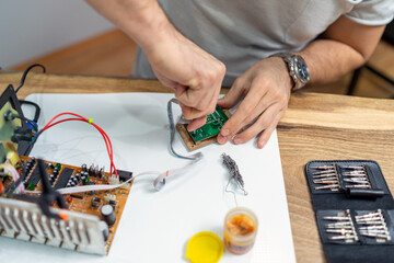 The young master electronics engineer checks, repairs and finishes the motherboard he was given to repair. He uses his tools and works in a home environment.