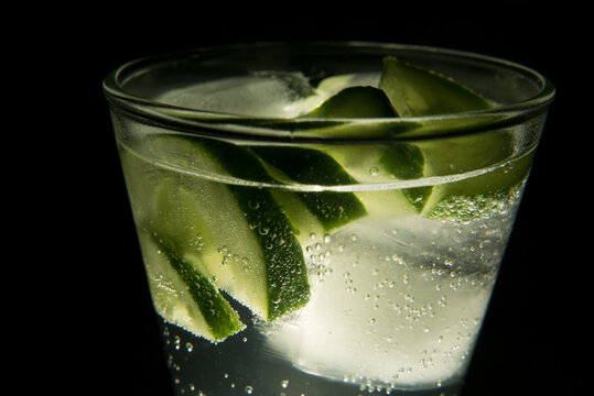 Glass of gin tonic with ice, cucumber, black background