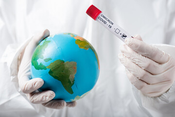 partial view of scientist in hazmat suit and latex gloves holding globe and positive covid-19...