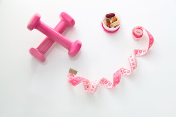 Pink dumbbells, supplements and spiral tape measure on white