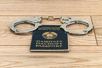 Passport of a citizen of the Republic of Belarus and handcuffs. Wooden background. Close-up.