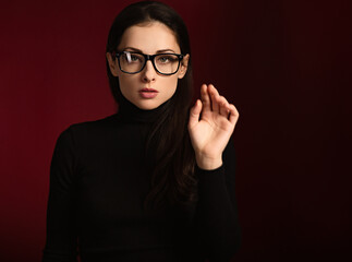 Business thinking woman in glasses find the answer in clever mind with with gestering the hand in black clothing on dark shadow red background. Closeup front