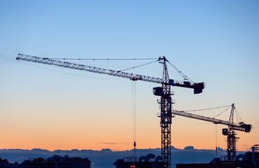 Silhouettes of tower cranes on construction site at sunset