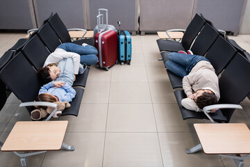 family sleeping on airport seats in departure hall.