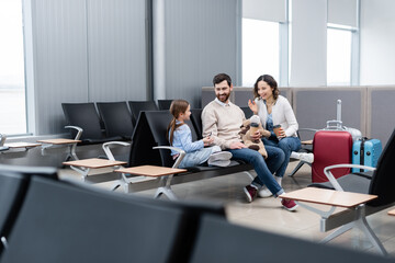 Fototapeta premium cheerful parents looking at daughter with smartphone in airport.