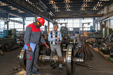 Fototapeta na wymiar Production Supervisor Talking To African American Worker Next To Train Wheels At Train Factory. Area For Maintenance, Repair And Service Of Trains And Wagons. 