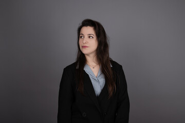 attractive confident brunette business woman in blue blouse and black jacket on grey background.