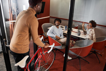 Fototapeta premium Stylish multiracial man entering with bike walking inside the coworking room