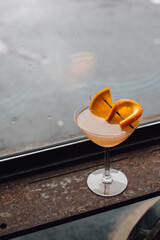 citrus orange grapefruit cocktail in coupe stem glass sitting by window