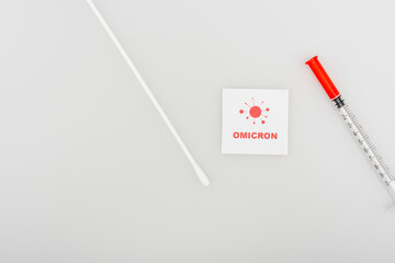 top view of card with red omicron lettering and bacteria icon near syringe and swab test on grey...