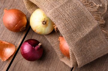 Red and white onions on a rustic wooden table spilling out of a cloth sack in the kitchen, top view. High quality photo