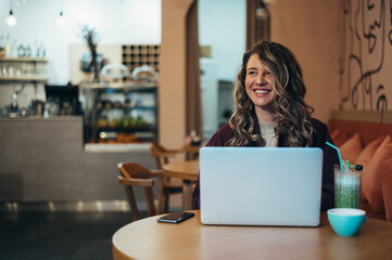 Beautiful young woman drinking coffee and working on her laptop in a cafe