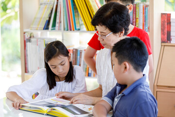 A Group of Asian Student Kid Reading a book with women teacher in School library with Shelf of Books in Background, Asian Kid Education Concept