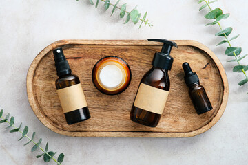 Top view set of SPA natural organic beauty products in amber glass containers on wooden plate with eucalyptus leaves.