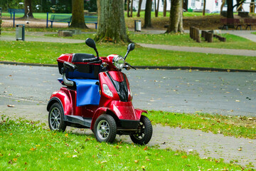 A four-wheeled red motor scooter standing on the side of the road.