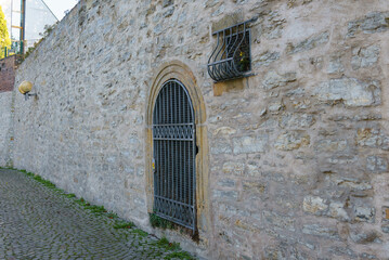 An ancient stone wall with a door and a small window, closed with wrought iron bars.
