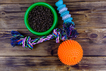 Bowl with pet food, dog toy for teeth cleaning, rope with tied knots and toy ball on a wooden background. Top view