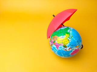 Red umbrella and world globe on a yellow background with copy space.
