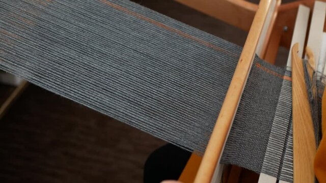 Weaver sends the thread through shed, takes the reed and tamps the yarn down. Weaving process, close up