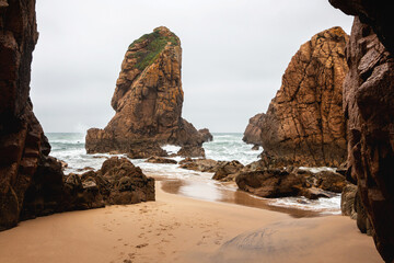 Fototapeta na wymiar Beautiful landscape on the Ursa beach with the sandy coast of the Atlantic Ocean, turquoise raging water among rocks and stones in cloudy weather, Portugal