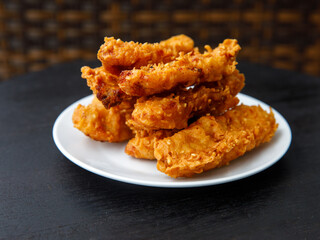deep-fried fritters sliced banana, also known as Kluay khek, served on white plate on black wooden table.
