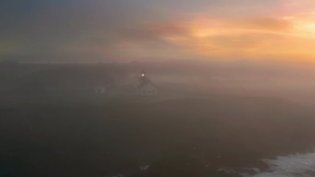 Point Cabrillo Light station coastal lighthouse at west coast of Unites States of America. Light comes from glass lantern lens illuminating thick morning fog above ocean at sunrise. Coastal lighthouse