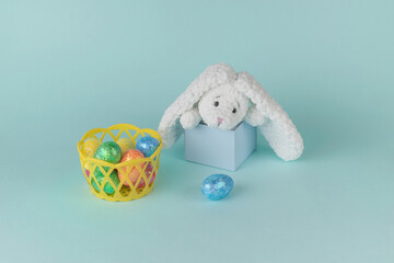 A basket with colorful Easter eggs and a bunny peeking out of a gift box.
