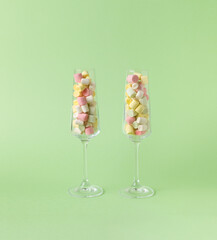 Two tall glass glasses filled with colorful marshmallows on a green background.