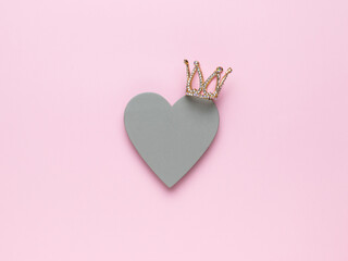 A golden crown and a gray wooden heart on a pink background. The concept of love and power. © kvladimirv