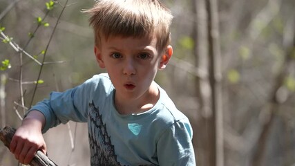 Little boy playing with a stick outdoors in the forest, slow motion.