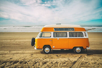 Vintage yellow van on the beach with cloudy sky on background, retro color effect, vacations concept