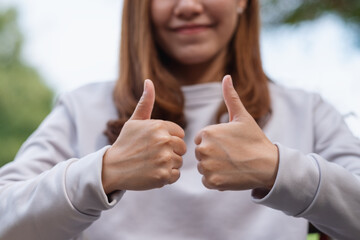Closeup of a young woman making and showing thumbs up hand sign