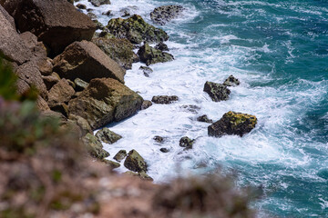 Sunny rocky shore with beautiful sea and sea foam in Nazaré, Portugal